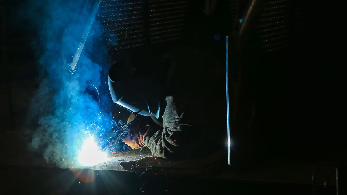 A welder in brown gloves and a mask welding as sparks and smoke rise