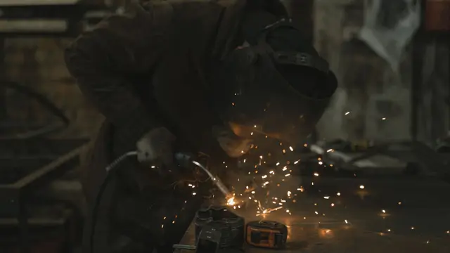 A welder in a safety jacket welding in a dimly lit workshop