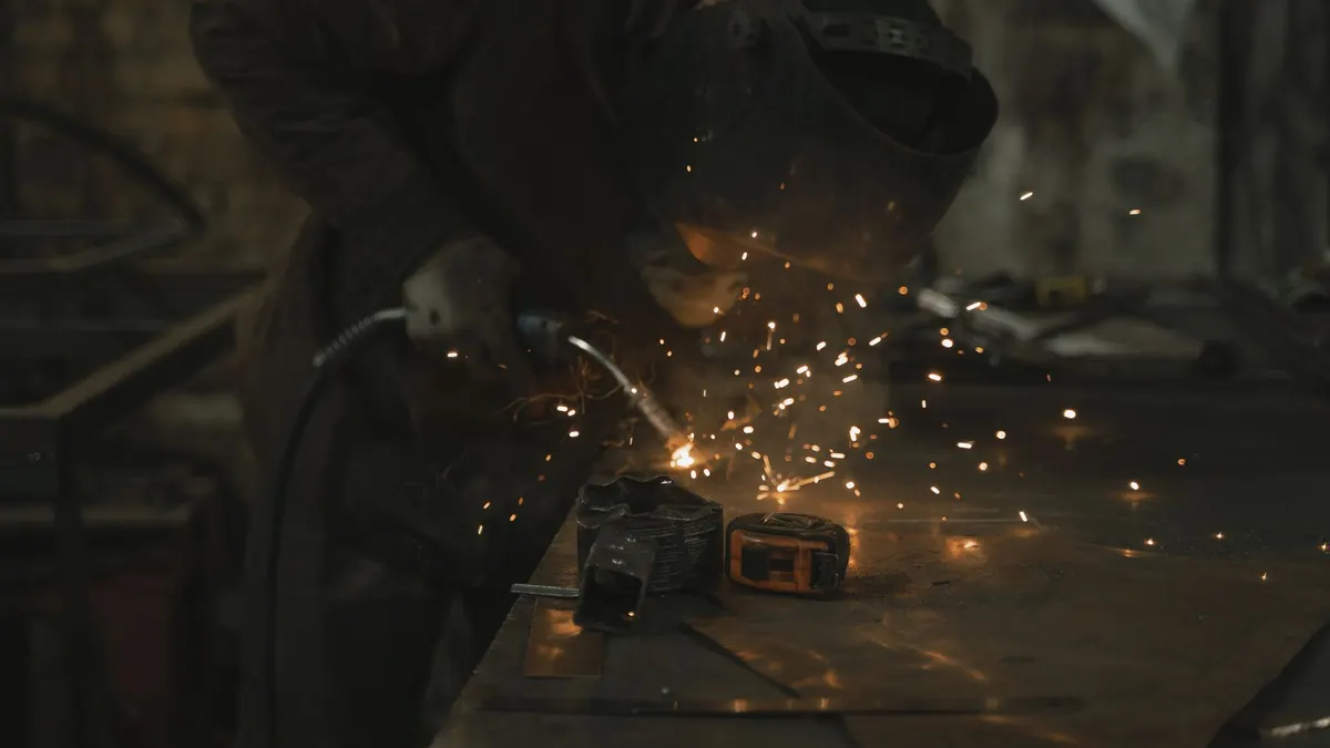 A welder in a safety jacket welding in a dimly lit workshop