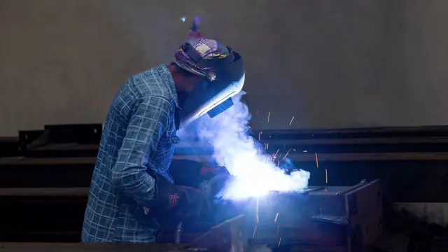 A welder in protective gear working with sparks in a factory