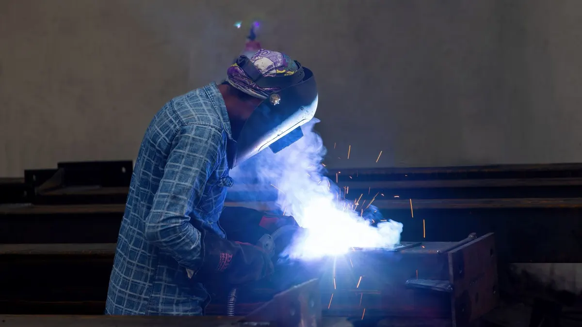 A welder in protective gear working with sparks in a factory