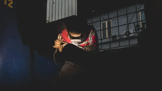 A welder working on a pipe at night in an industrial yard