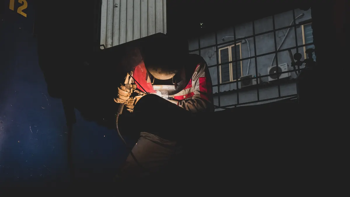 A welder working on a pipe at night in an industrial yard