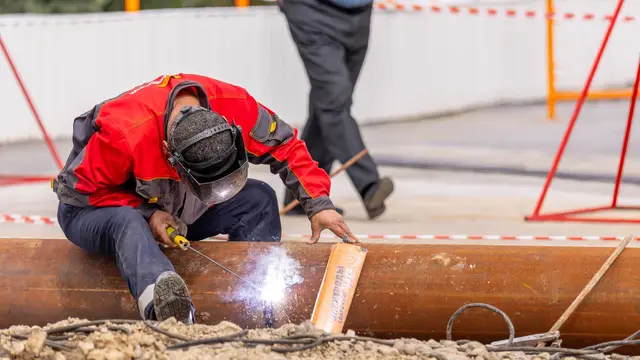 A worker in a red jacket welding a large pipe at a construction site