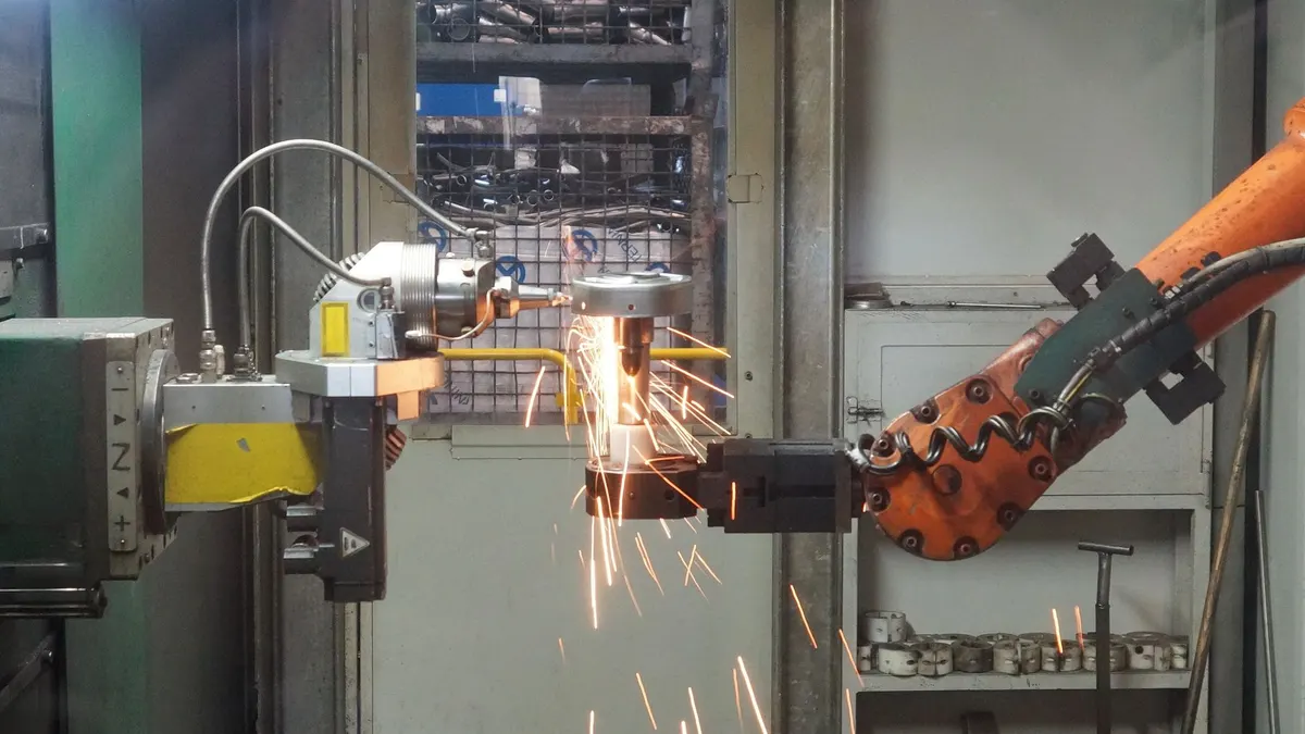 An orange robotic arm welding in a factory cell as sparks fly