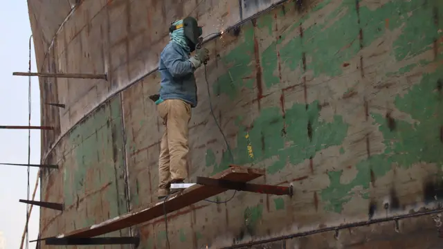 A worker welding the hull of a large ship outdoors