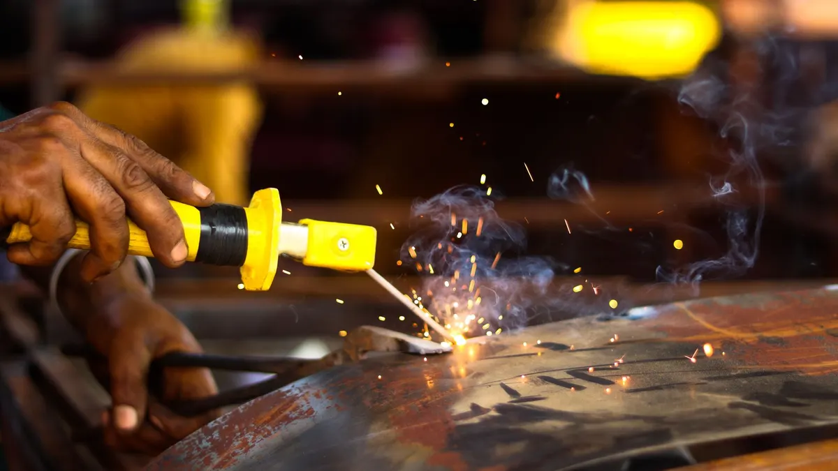 A welder's hands guiding a torch across metal as sparks fly