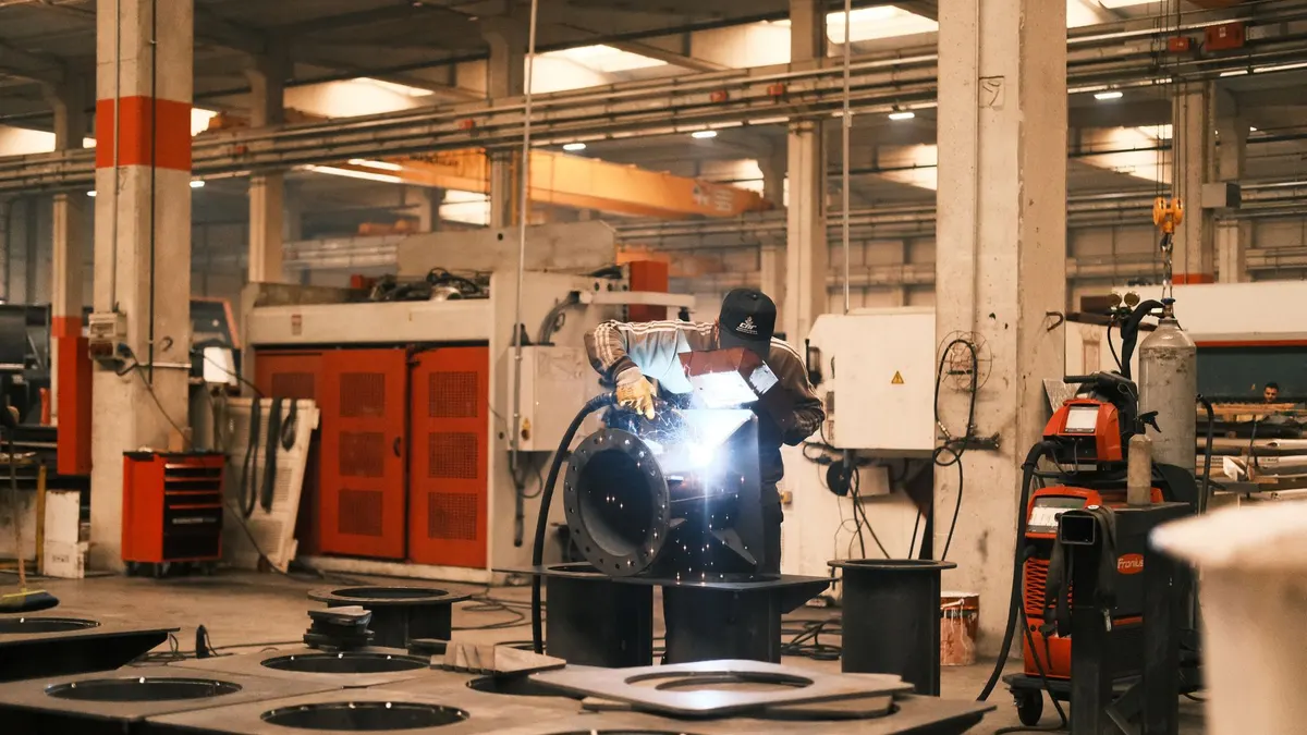 A welder working on large metal components in a factory