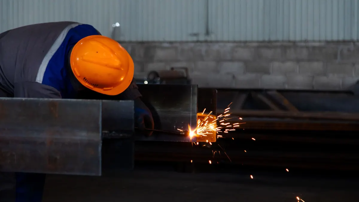 A welder in a hard hat welding a steel beam in a factory