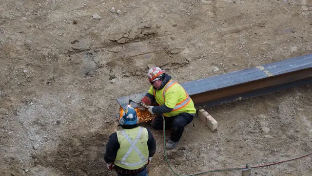 Two construction workers in safety vests welding steel at a site