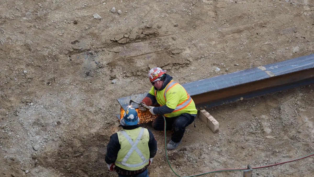 Two construction workers in safety vests welding steel at a site