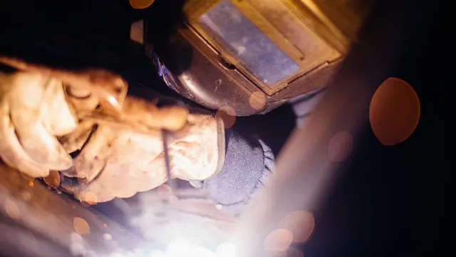 Close-up of a welder's helmet and gloves as sparks light the joint