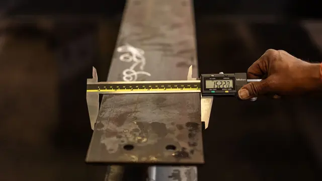 A worker measuring a steel beam with a digital caliper