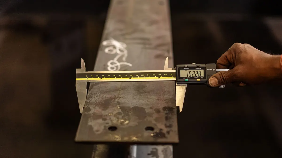 A worker measuring a steel beam with a digital caliper
