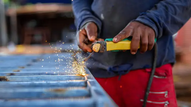 A welder working a torch across a steel grate outdoors as sparks spray