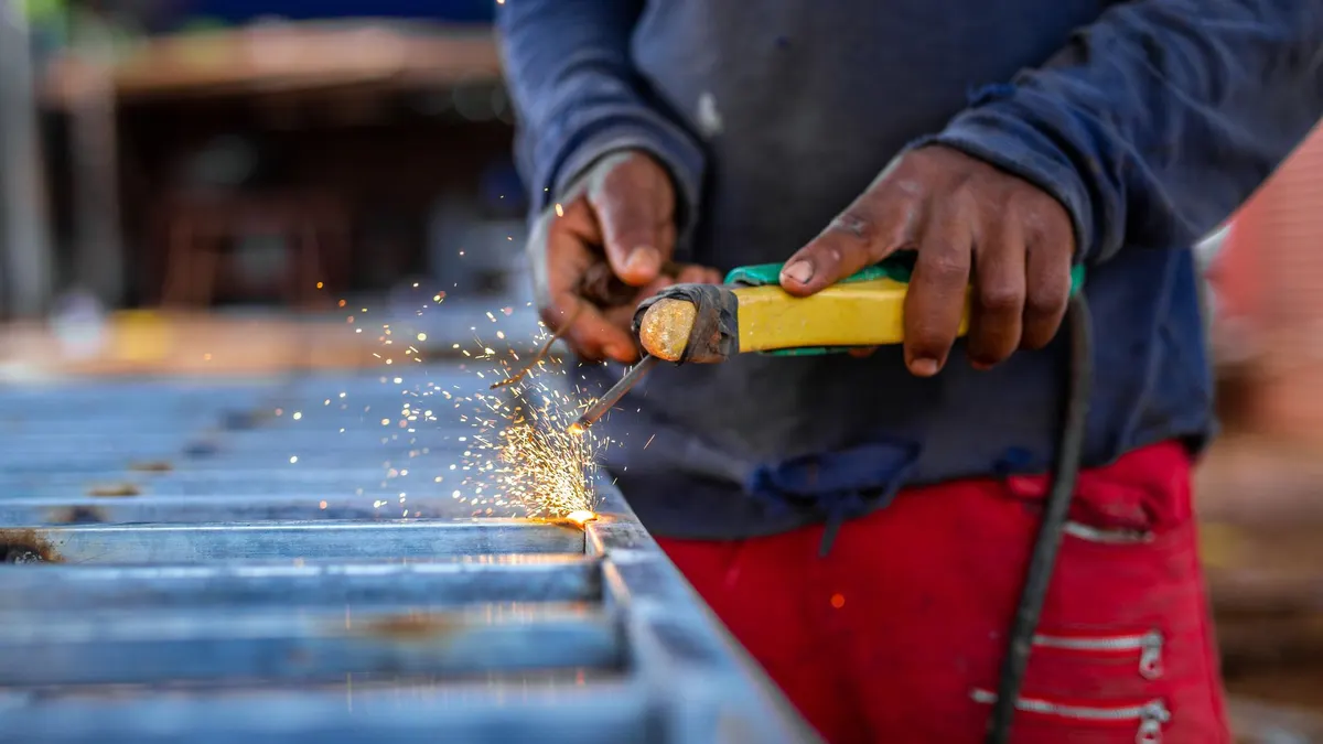 A welder working a torch across a steel grate outdoors as sparks spray
