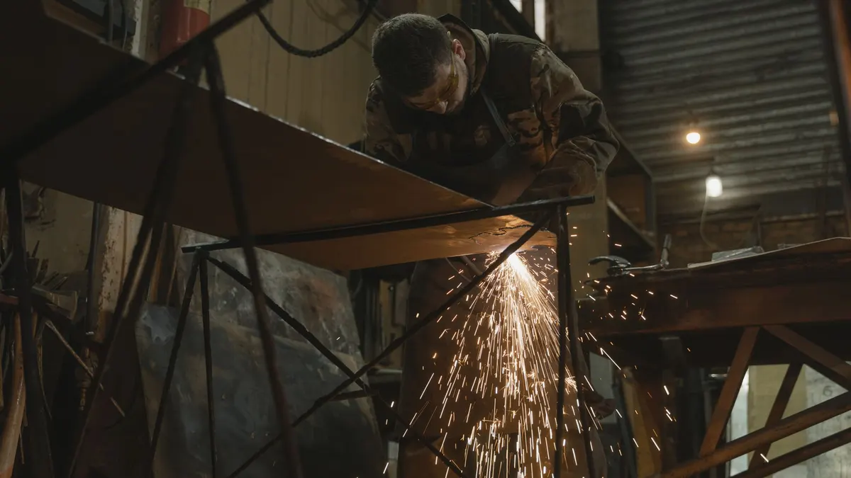 A welder in safety glasses welding a metal bar as sparks fly