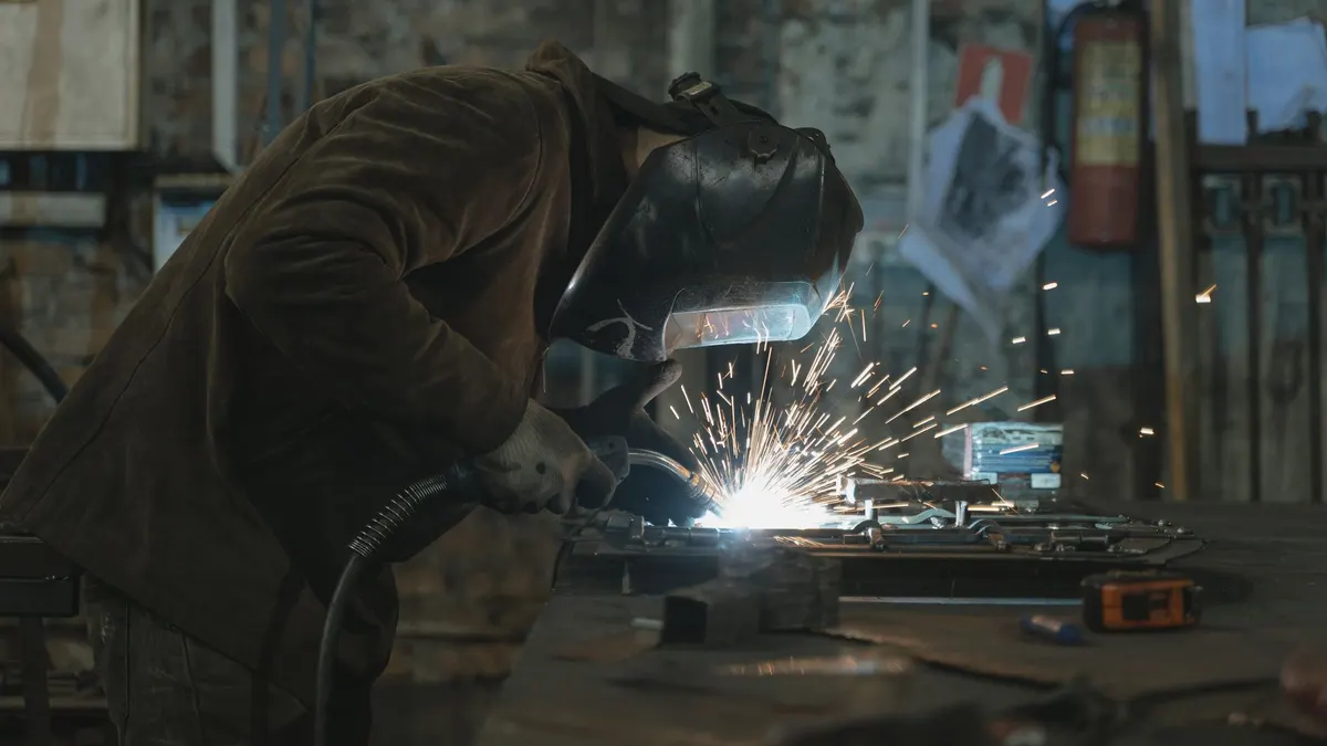 A welder at a workbench welding a metal piece with sparks flying