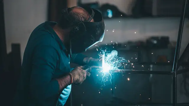 Close-up of a welder in a helmet running a bead in blue light
