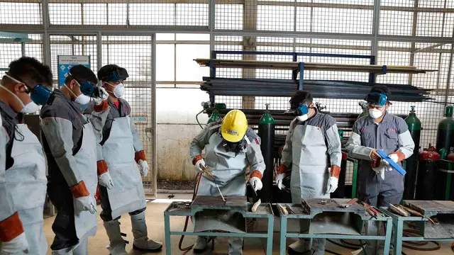 Welding students in protective jackets and respirators at the booths of a training shop