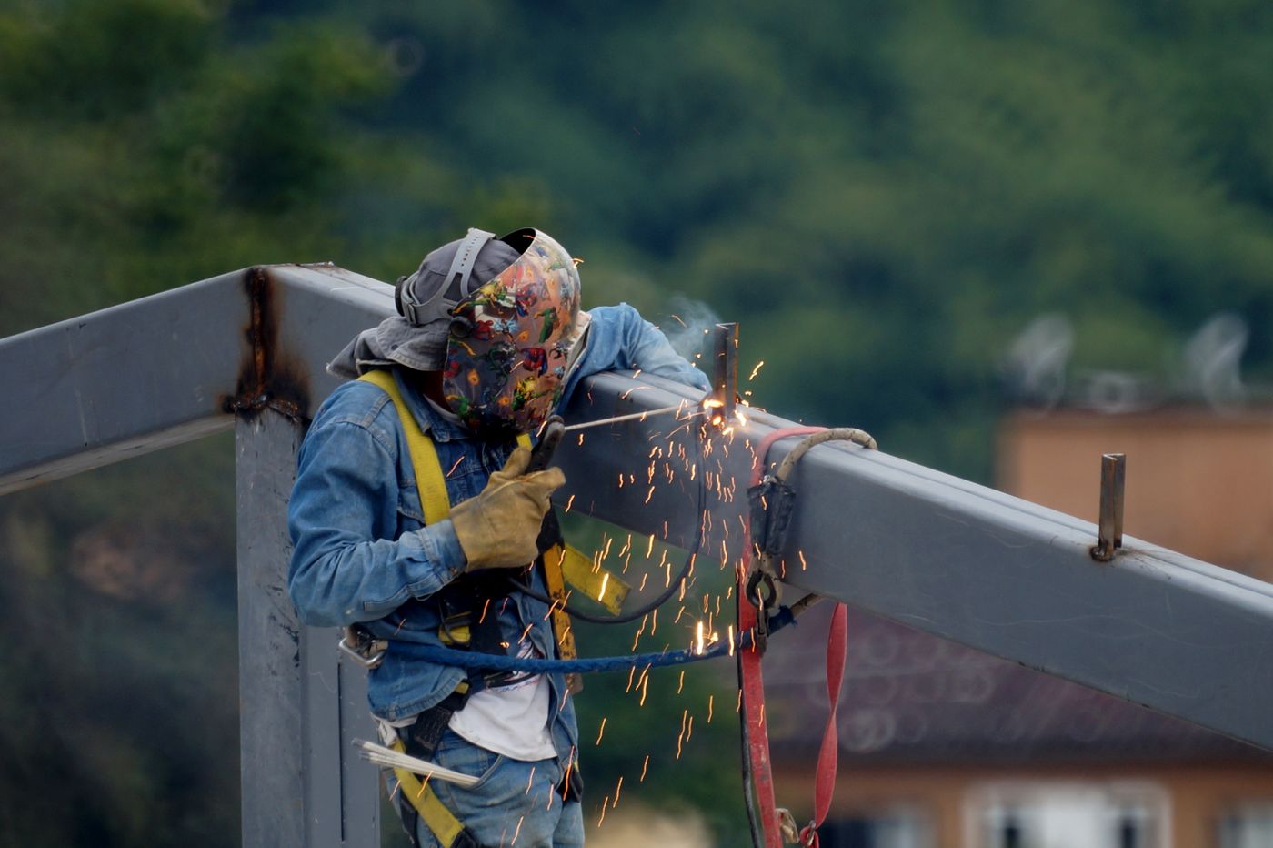 A welder in a harness stick-welding a steel beam outdoors